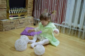 One year old baby girl sitting on the floor. A child playing with wicker balls. A blonde girl.