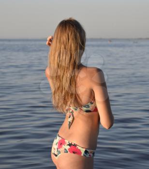 Blond girl in a bikini standing in the sea water. Beautiful young woman in a colorful bikini on sea background.