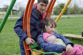 Young married couple with child in playground. Young family on a swing.