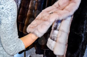 The girl touches the fur on the fur coat. Choosing a fur coat in the store.