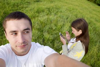 A man with a woman in a meadow. Selfi does the guy and the girl looks at the smartphone screen.