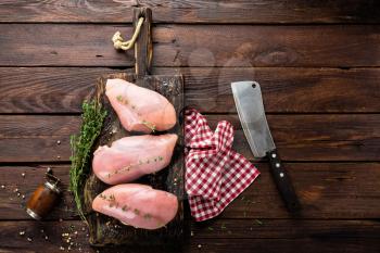 Raw chicken breasts fillets with thyme and spices on wooden cutting board on rustic background copy space directly above