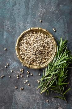 White pepper and fresh rosemary twigs, culinary ingredients on dark background, copy space