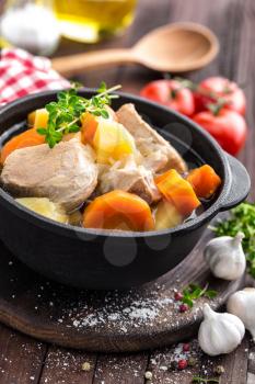 Meat stewed with carrots and potatoes in sauce on wooden rustic background