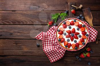 Delicious strawberry pie with fresh blueberry and whipped cream on wooden rustic table, cheesecake, top view