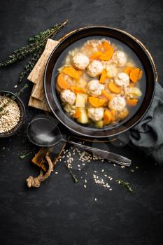 Fresh vegetable soup with meatballs and pearl barley in bowl on black background. Top view