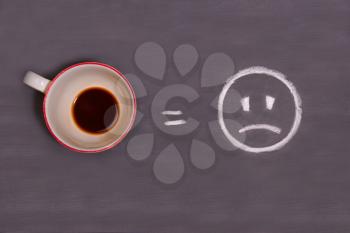 A cup of coffee and sad smiley drawn with chalk on the table. Energy from coffee.