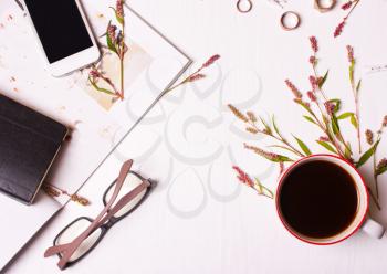 Top view of designer table, a woman with a cup of coffee, magazine, phone, glasses, rings, flowers and a notepad.Workspace.Working.