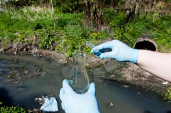 Check the water sample for Hand in a glove with a bulb and a test tube against the background of a sewer pipe, dirty water. Pollution of ecology, environment