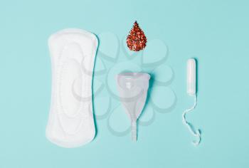 Tampon, Pad, menstrual cup with a drop of blood on a blue background. The view is flat. Concept of critical days, menstruation