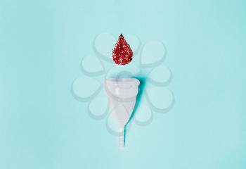 white menstrual cup  with a drop of blood on a blue background. Concept of women's health, hygienic means of protection, menstruation, ecology of the planet.