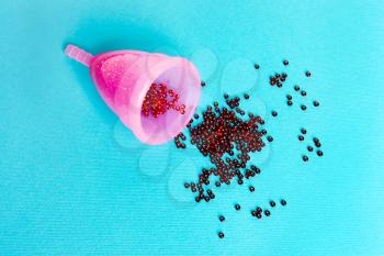 pink menstrual cup  with a drop of blood on a blue background. Concept of women's health, hygienic means of protection, menstruation, ecology of the planet.
