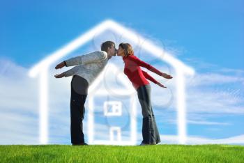Happy couple husband and wife making hands made house surrounded by the form of a house on a green meadow. Conceptual design.