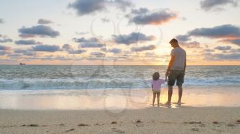 Father and daughter standing together on the sea beach at sunset. Emotional scene.
