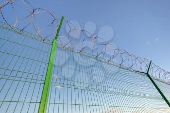 Slatted fence with barbed wire on top. Sky background behind Imprisonment concept.