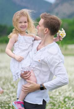 Happy father and daughter in big camomile mountain meadow. Emotional, love and care scene.