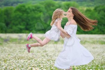 Happy mother and daughter play in big camomile mountain meadow. Emotional, love and care scene.