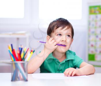 Little boy is drawing on white paper using color pencils