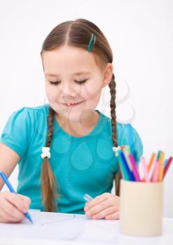 Little girl is drawing using color pencils while sitting at table