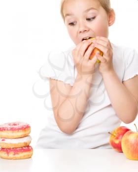 Cute little girl choosing between apples and cake, isolated over white