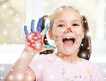 Portrait of a cute cheerful girl showing her hands painted in bright colors, over snowy background