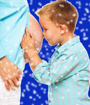 Happy child holding belly of pregnant woman, over blue snowy background