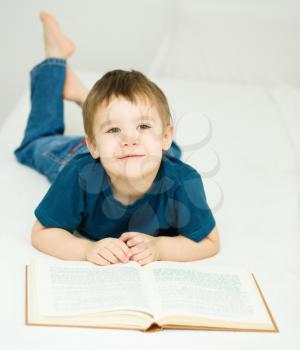 Cute little boy is reading book while sitting at table, indoor shoot