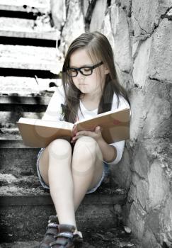 Cute little girl is reading a book outdoors