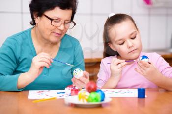 Grandmother with her granddaughter are coloring eggs for Easter, indoors
