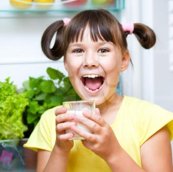 Happy girl drink milk standing near refrigerator with fruits and vegetables