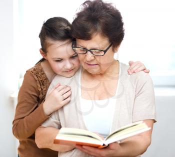 Cute grandmother is reading book with her granddaughter, in home