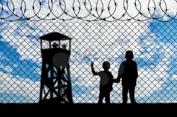 Refugee children concept. Silhouette of two children of refugees near the border on the background of a watchtower