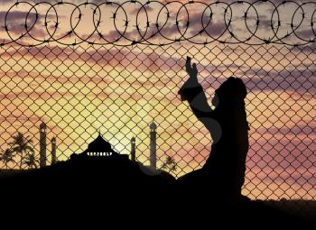 Islamic religion. Muslim Praying near the fence of barbed wire on the background of the mosque