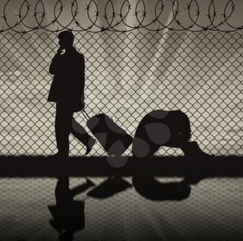 Concept of the refugees. Silhouette of a couple of refugees near the border fence at sunset and reflection