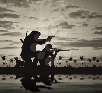 Concept of terrorism. Silhouette of a terrorists with a rifle on a background of sunset and palm trees and reflection