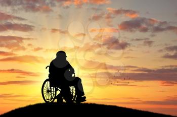 Concept of disability and old age. Silhouette of disabled person in a wheelchair on the sunset background
