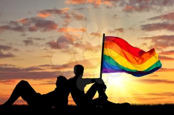 Concept of gay people. Silhouette of two gay vacationers at sunset and rainbow flag