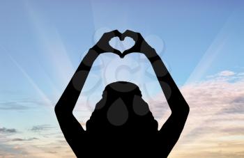 Concept of love. Silhouette of a girl showing her hands heart symbol love at sunset