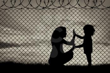 Concept of refugee. Silhouette of mother and child refugees at the border fence at sunset