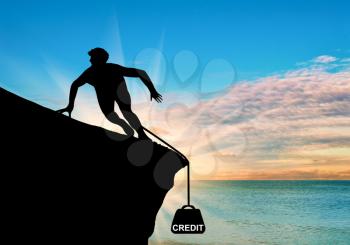 Concept of money. Silhouette of a man on a rock and a credit in the form of cargo on sea sunset background