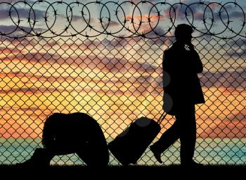 Concept of the refugees. Silhouette of a couple of refugees near the border fence at sunset