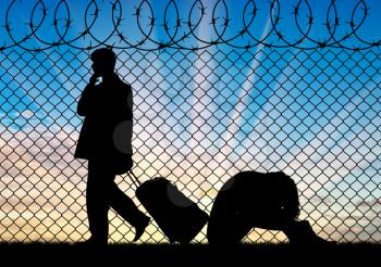Concept of the refugees. Silhouette of a couple of refugees near the border fence at sunset