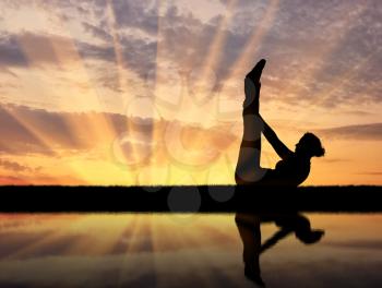 Concept of meditation and relaxation. Silhouette of a girl practicing yoga at sunset and reflection in water