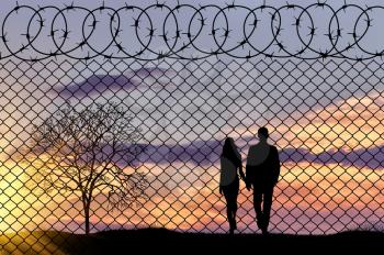 Concept of refugee. Silhouette family of refugees near the border fence in the sunset