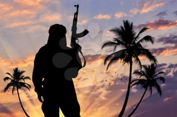 Silhouette of a terrorist with a weapon against a background of a sunset with palm trees