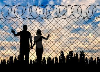 Concept of the refugees. Silhouette of refugee families near the fence on the background of the city and sunset