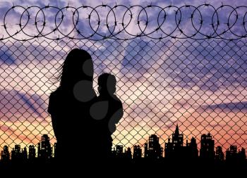 Concept of the refugees. Silhouette refugee mother with a baby in the background of the fence and the city at sunset
