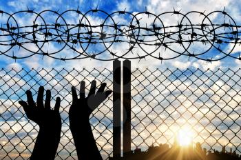 Concept of religion is Islam. Silhouette of hands facing the sky against a background of a fence with barbed wire and the city