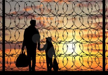 Concept of refugee. Silhouette of a family with a child refugee father near the fence with barbed wire at sunset
