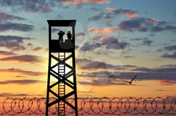 Concept of security. Silhouette barbed wire and a watchtower with soldiers at sunset